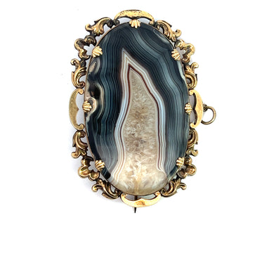An ornate jewelry piece, this Victorian 10ktyg banded agate and quartz crystal pendant/pin features an oval banded agate centerpiece with multicolored layers in green, blue, and white. Set in an intricate gold-toned frame with decorative floral and scroll motifs, the pin and clasp are visible on the back.