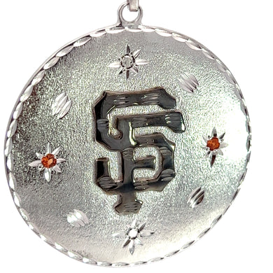 A close-up of the Late Century 14ktwg Custom Made SF Giants .20cttw Orange Sapphire + .20cttw Black Diamond Pendant, showcasing an embossed, intertwined 'SF' logo in the center. The pendant features a textured background with star-like embellishments and is adorned with two small orange sapphires. The edge of this personalized accessory boasts a scalloped design.