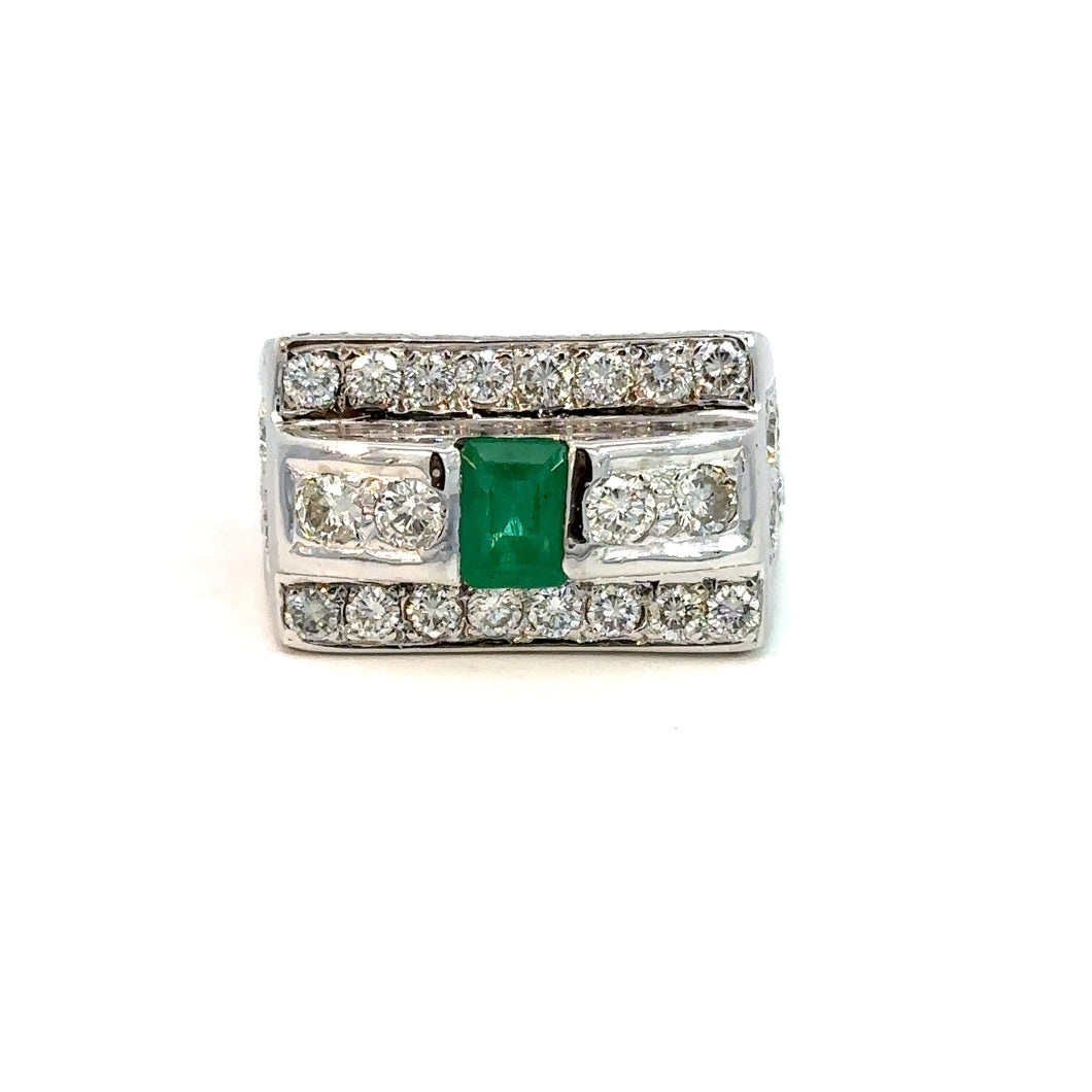 A striking Late Century 14kt white gold ring featuring a central 1ct emerald-cut emerald, flanked by two smaller diamonds. The broad band is adorned with rows of small diamonds on the top and bottom edges, contributing to its ornate design. This Emerald and Diamond Ring, set against a plain white background, showcases a total diamond weight of 5.70 carats in round brilliant cuts.
