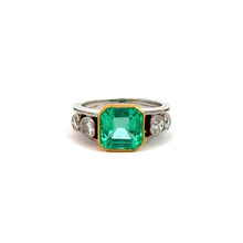 Load image into Gallery viewer, Mid Century Platinum &amp; 18kt Yellow Gold 4.03 Emerald Cut Emerald + .70cttw Diamond Ring exudes sophisticated elegance with its stunning 4ct emerald-cut green gemstone, set in a luxurious blend of platinum and 18kt yellow gold. Each side is gracefully flanked by two round white diamonds, creating a perfectly symmetrical design against the white background.