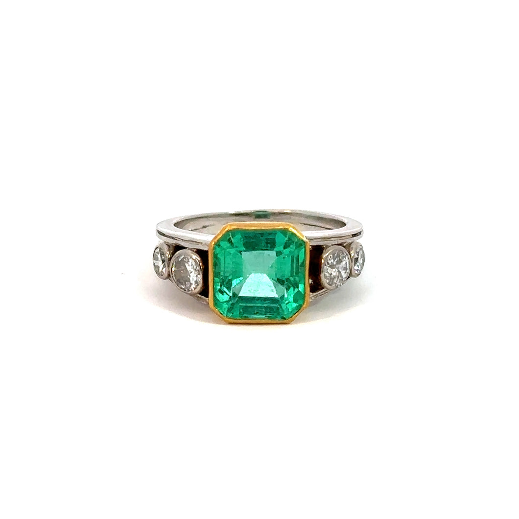 Mid Century Platinum & 18kt Yellow Gold 4.03 Emerald Cut Emerald + .70cttw Diamond Ring exudes sophisticated elegance with its stunning 4ct emerald-cut green gemstone, set in a luxurious blend of platinum and 18kt yellow gold. Each side is gracefully flanked by two round white diamonds, creating a perfectly symmetrical design against the white background.