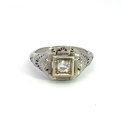 A captivating piece, the Art Deco 18ktwg .20ct Old Mine Cut Diamond Ring boasts an exquisite filigree design in 18kt White Gold. The centerpiece is a single round Old Mine Cut Diamond securely set within a square bezel on the front. Displayed gracefully against a plain white background, this ring exudes timeless elegance.