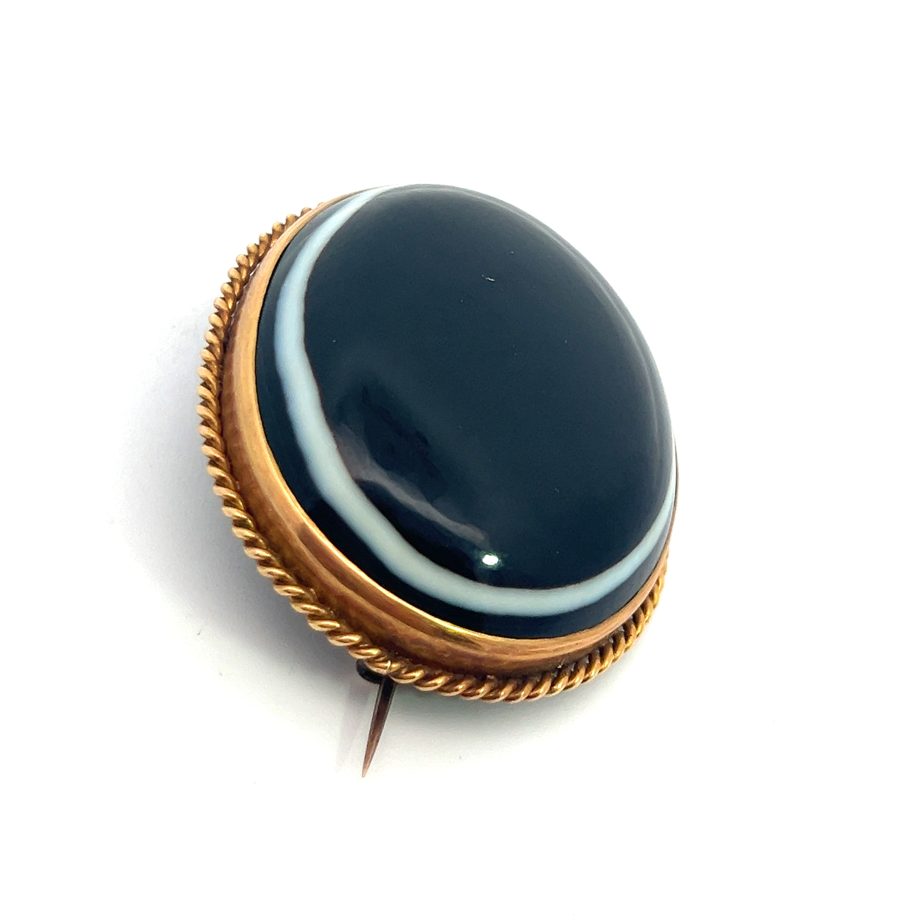 The Victorian 22kt Yellow Gold Bullseye Agate Brooch showcases a polished black onyx stone, elegantly encased in a golden, rope-style border. Crafted from 22kt yellow gold, it features a simple pin clasp at the back for fastening.