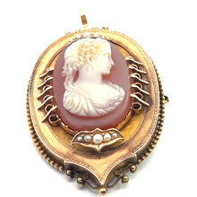 Load image into Gallery viewer, The Victorian 14ktyg Carved Agate Portrait of a Lady Cameo is an antique brooch showcasing a carved agate portrait cameo of a woman in relief against a reddish-pink background. The frame features intricate 14kt yellow gold filigree and is adorned with small pearls, creating a timeless and elegant design. The brooch is equipped with a pin and clasp at the back.