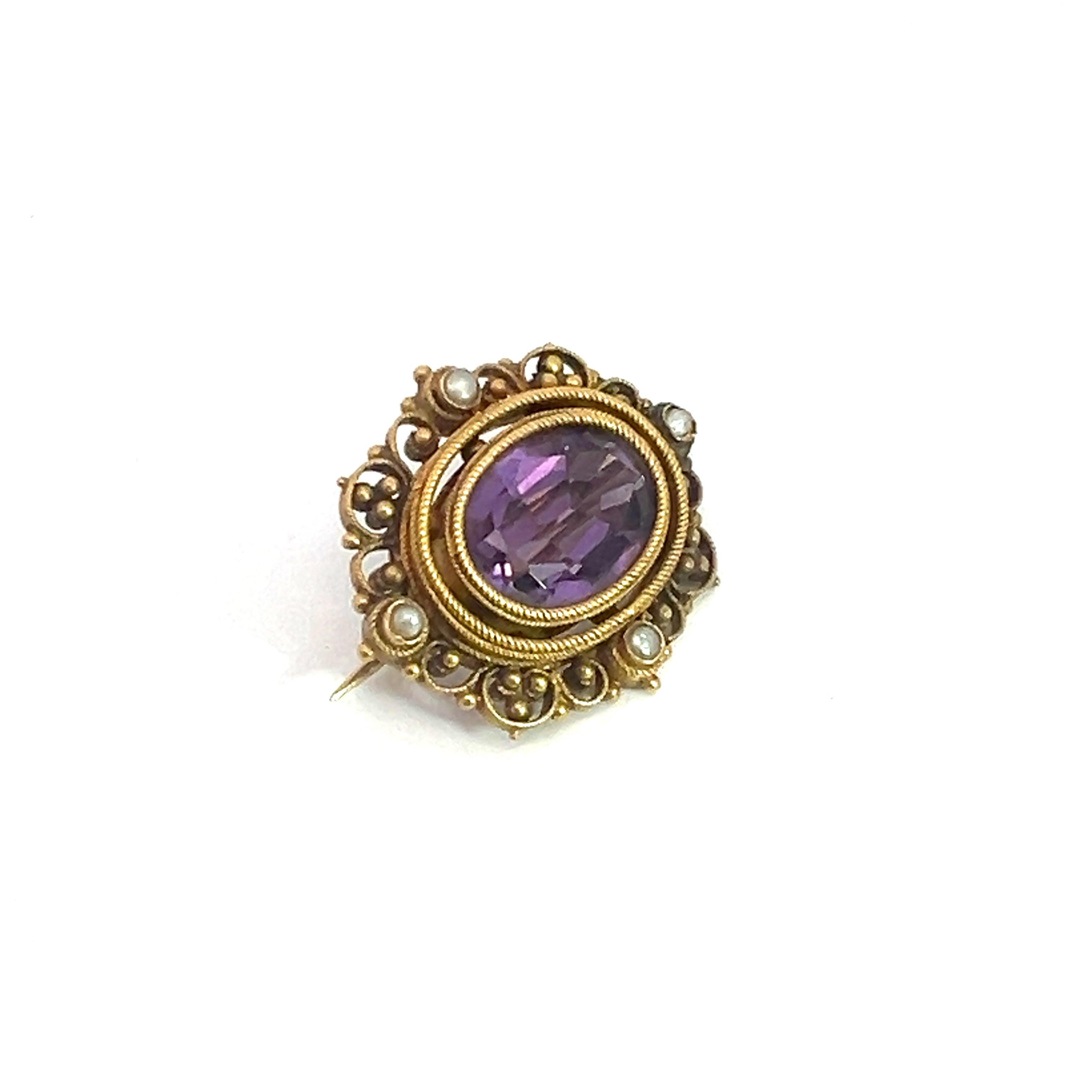 The Victorian 14ktyg 4.70ct Amethyst + seed pearl pin is an elegant oval brooch featuring a central amethyst gemstone enveloped by intricate 14kt yellow gold filigree and delicate seed pearls, set against a white background.