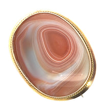 Load image into Gallery viewer, A detailed image showcasing the Victorian 14ktyg Large Banded Agate Pin, highlighting its oval-shaped, polished banded agate stone with intricate layers of pink, white, and brownish hues. The gemstone is elegantly set in a 14kt yellow gold bezel adorned with a twisted rope border design.