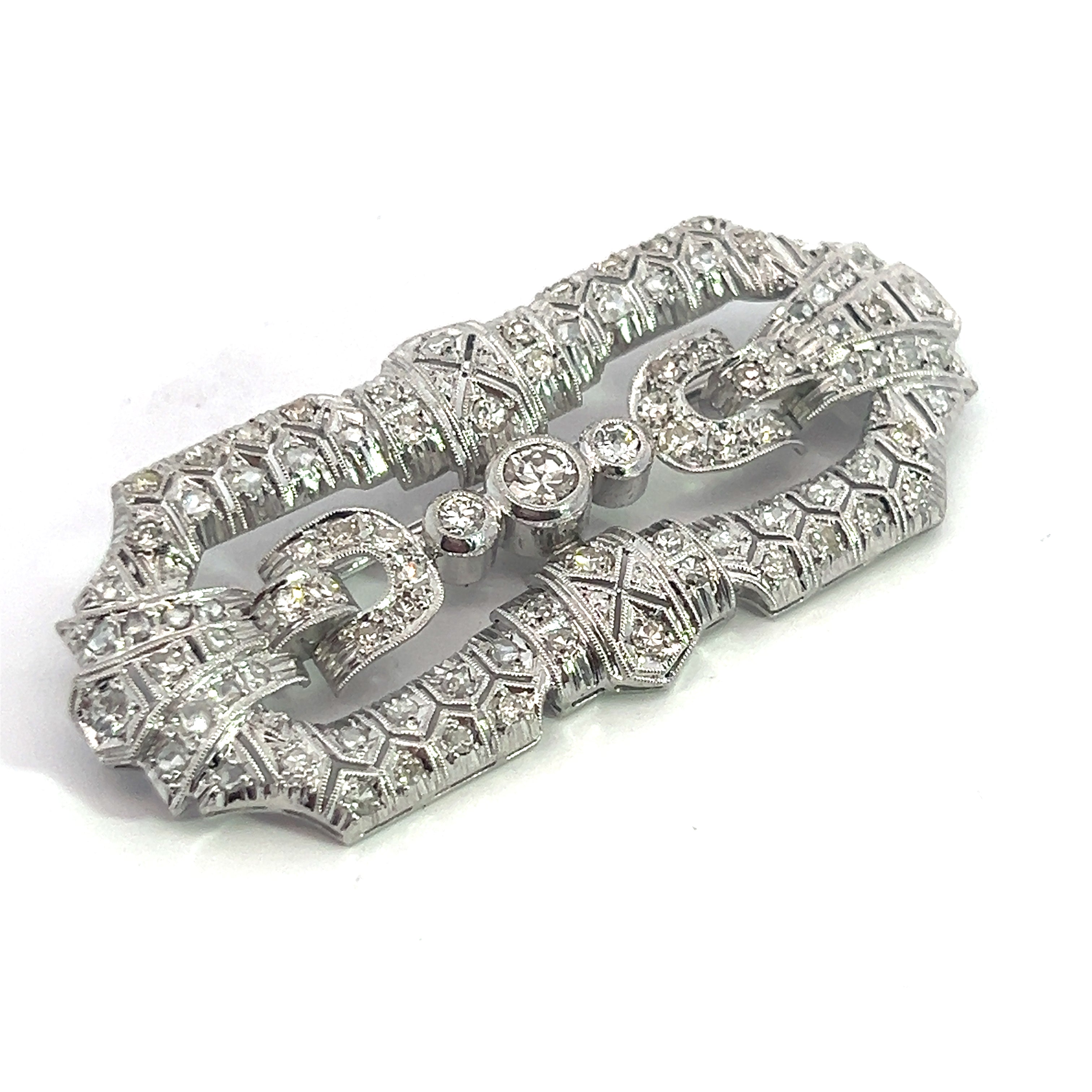 An intricately designed Art Deco Platinum Brooch featuring 3.65cttw of Old Euro, Old Mine, and Antique Cut Diamonds. The brooch showcases geometric patterns and a symmetrical, ornate structure with a central clasp, exuding vintage elegance through its detailed craftsmanship.