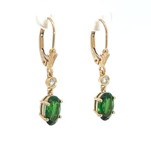 Load image into Gallery viewer, A pair of the Modern 14kt Yellow Gold 2.25ct Tsavorite Garnets + .10cttw Diamond Earrings, featuring oval-cut tsavorite garnets secured by prongs with a small round diamond accent above each gem, attached to leverback clasps on a white display stand against a plain white background.