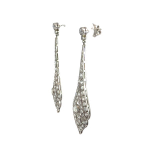 A pair of elegant, long Art Deco Platinum 8cttw Old Mine Cut & Antique Cut Diamond Drop Earrings encrusted with diamonds. The earrings feature an intricate, tapering design with a mix of round and baguette-shaped diamonds set in platinum. The stud backing is visible.