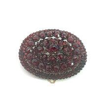 Load image into Gallery viewer, The Victorian Vermeil Oval Garnet Brooch is an ornate piece adorned with clusters of deep red garnet gemstones arranged in concentric patterns. The brooch features a dense and intricate design, with varying sizes of garnets covering the entire surface, exuding vintage charm. A small gold clasp is visible at the bottom edge.