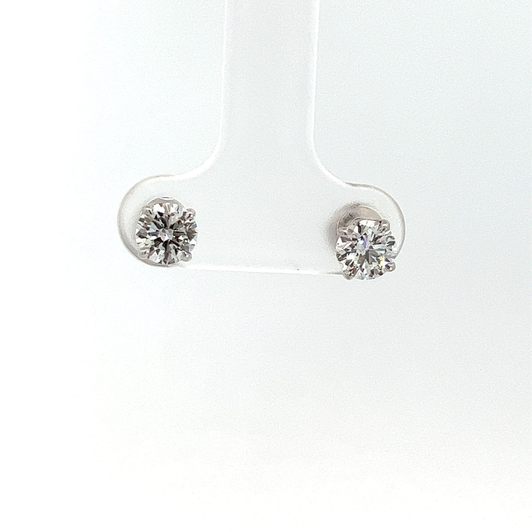 A pair of Modern 14kt White Gold 1.01 Round Brilliant Cut Diamond G-H VS Stud Earrings mounted on a transparent display stand. The diamonds, set in 14kt white gold prongs, reflect light to showcase their brilliance. With a minimalist white background, the elegant simplicity of the design is highlighted beautifully.