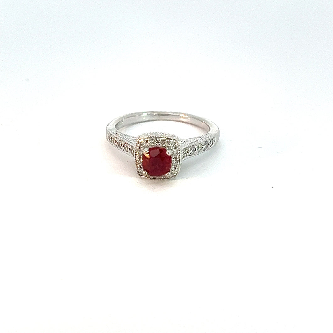 The Modern 14kt White Gold 1ct Ruby + .50cttw Diamond Ring showcases a vibrant red ruby gemstone at its center, surrounded by a halo of sparkling white diamonds. The band is also embellished with small diamonds, adding extra brilliance to the sophisticated design. The ring is beautifully displayed against a plain white background.