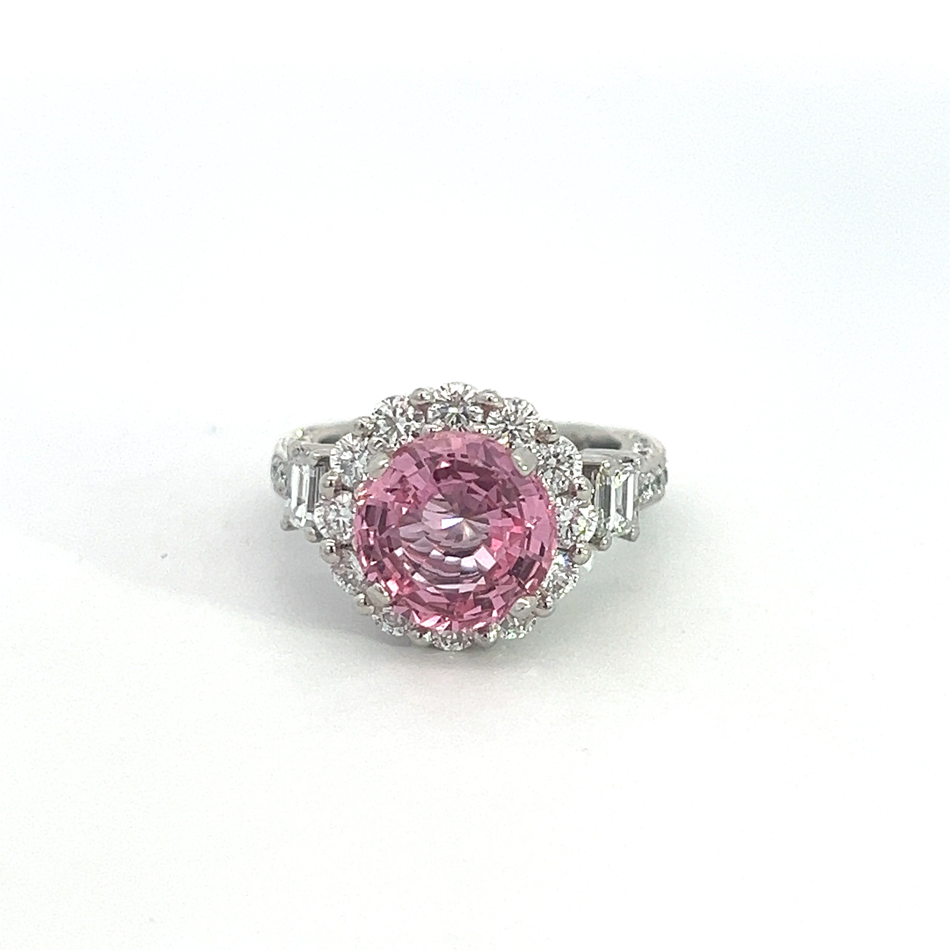 Introducing the "Modern Platinum 3.30 No Heat Padparadscha Sapphire" ring, showcasing a stunning large, round no-heat Padparadscha sapphire at its center. This exquisite gemstone is encircled by a halo of small, sparkling diamonds. The platinum band is further embellished with additional diamonds on either side, enhancing its elegant and luxurious appeal.