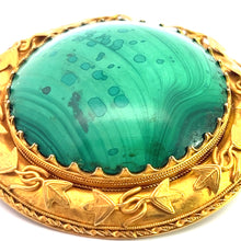 Load image into Gallery viewer, A close-up of the Victorian 18ktyg Fancy Frame Malachite Brooch featuring a large, round green malachite gemstone with natural marbling patterns. The gemstone is set in an ornate gold setting with detailed leafy designs and intricate borders, giving the brooch an antique, elegant appearance.